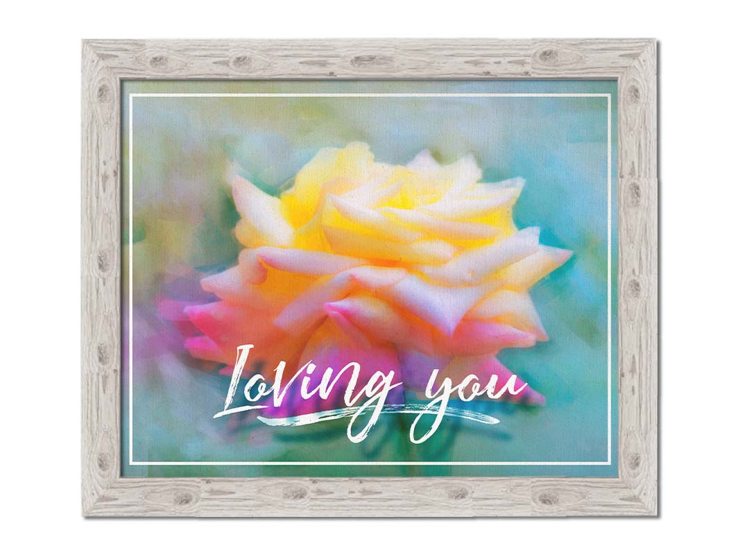 A photo of a pink and yellow rose against a blue background, edited to have a painterly appearance. It is overlaid with a white border and text reading "Loving you." Printed on canvas and framed.