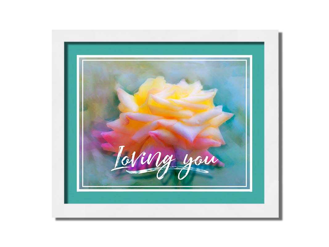 A photo of a pink and yellow rose against a blue background, edited to have a painterly appearance. It is overlaid with a white border and text reading "Loving you." Printed on paper, matted, and framed.