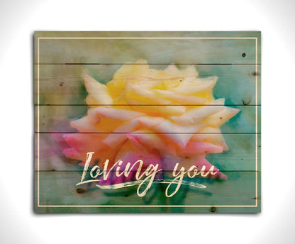 A photo of a pink and yellow rose against a blue background, edited to have a painterly appearance. It is overlaid with a white border and text reading "Loving you." Printed on a wood pallet.