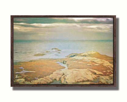 A photo of a stoney shore, looking out to sea under a cloudy sky. Printed on canvas in a float frame.