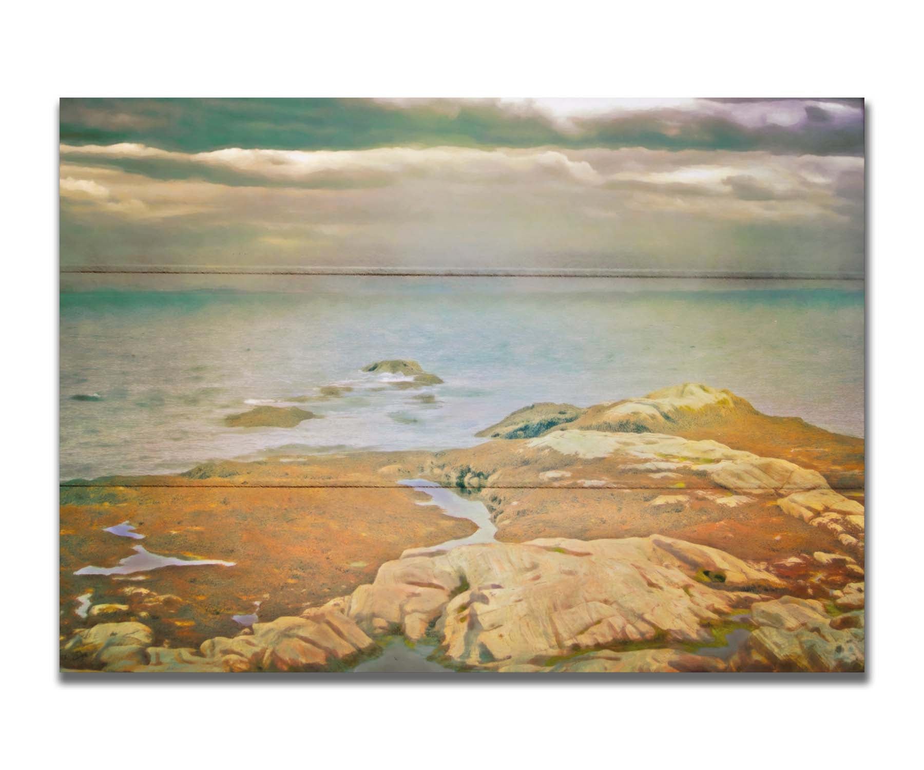 A photo of a stoney shore, looking out to sea under a cloudy sky. Printed on a box board.