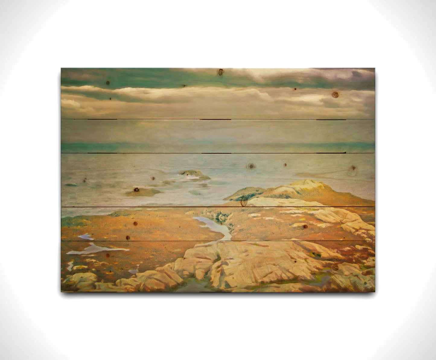 A photo of a stoney shore, looking out to sea under a cloudy sky. Printed on a wood pallet.