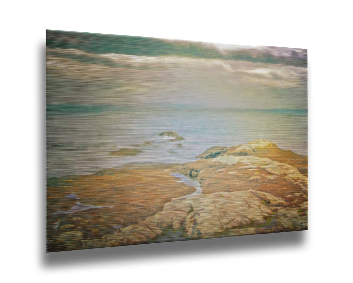 A photo of a stoney shore, looking out to sea under a cloudy sky. Printed on metal.