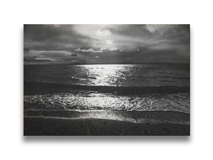 A photograph of the sea at night in grayscale. The light from the moon rerflects off the water in sharp contrast through the darkness of night. Printed on canvas.