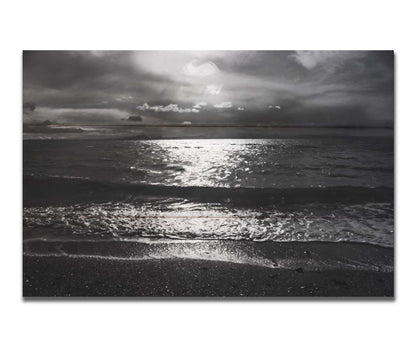 A photograph of the sea at night in grayscale. The light from the moon rerflects off the water in sharp contrast through the darkness of night. Printed on a box board.