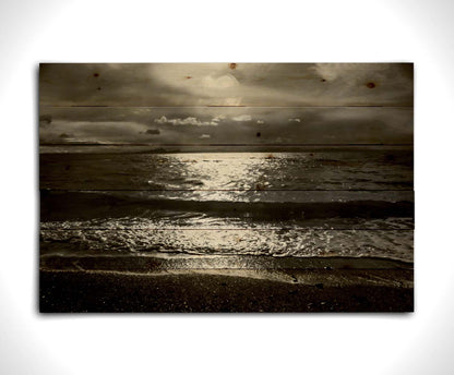 A photograph of the sea at night in grayscale. The light from the moon rerflects off the water in sharp contrast through the darkness of night. Printed on a wood pallet.