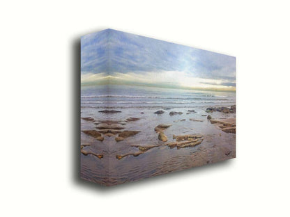 A photograph of the rocky shore of the North Sea at low tide. The sun peeks over the horizon through the partly cloudy sky. Printed on canvas.