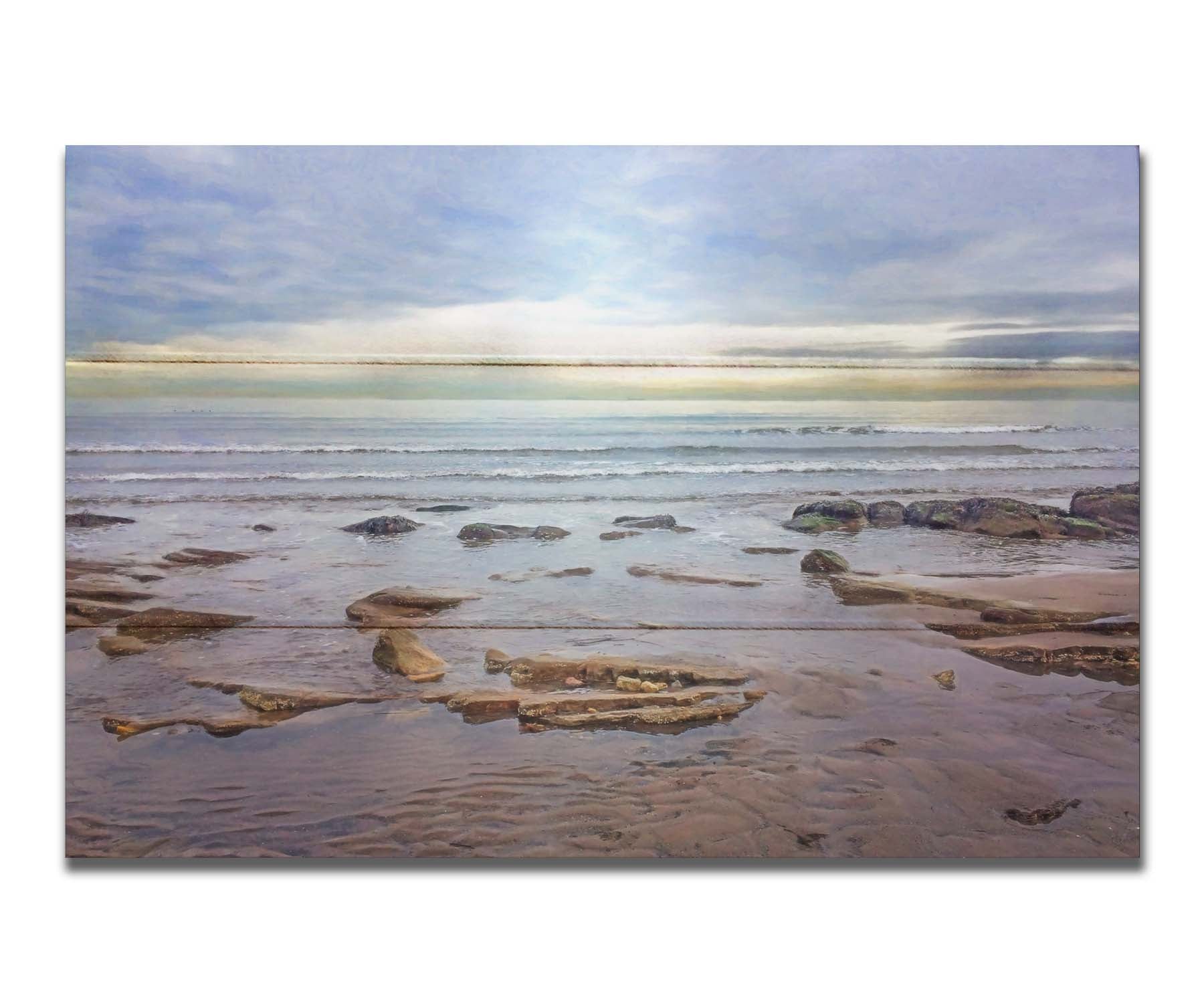 A photograph of the rocky shore of the North Sea at low tide. The sun peeks over the horizon through the partly cloudy sky. Printed on a box board.