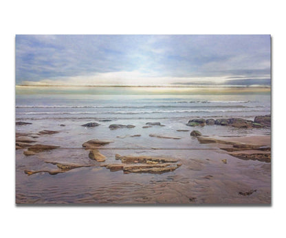 A photograph of the rocky shore of the North Sea at low tide. The sun peeks over the horizon through the partly cloudy sky. Printed on a box board.