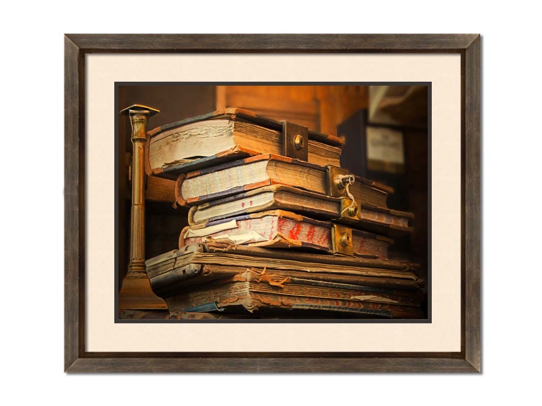 A photo of a stack of worn books, many bound shut by brassy locks. Printed on paper, matted, and framed.