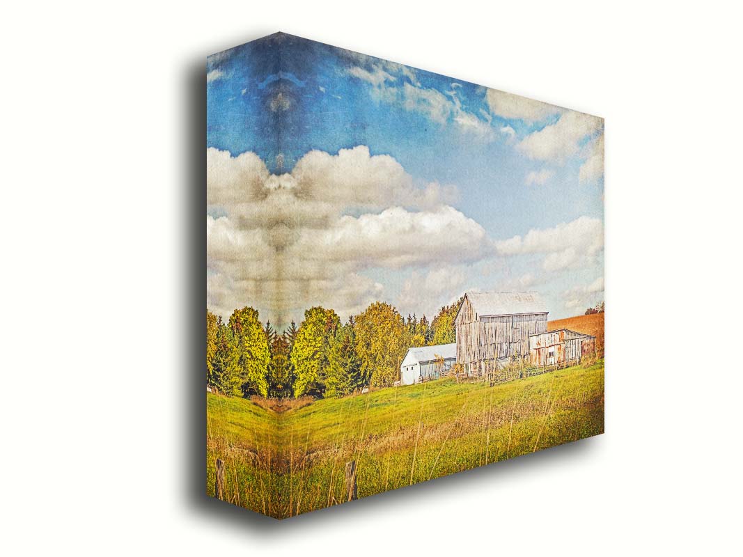 A photo of several barns, their associated pastures, and fields. The early signs of fall are present in the steadily changing leaves and crops. The sky above is wide, blue, and populated with fluffy clouds. Printed on canvas.