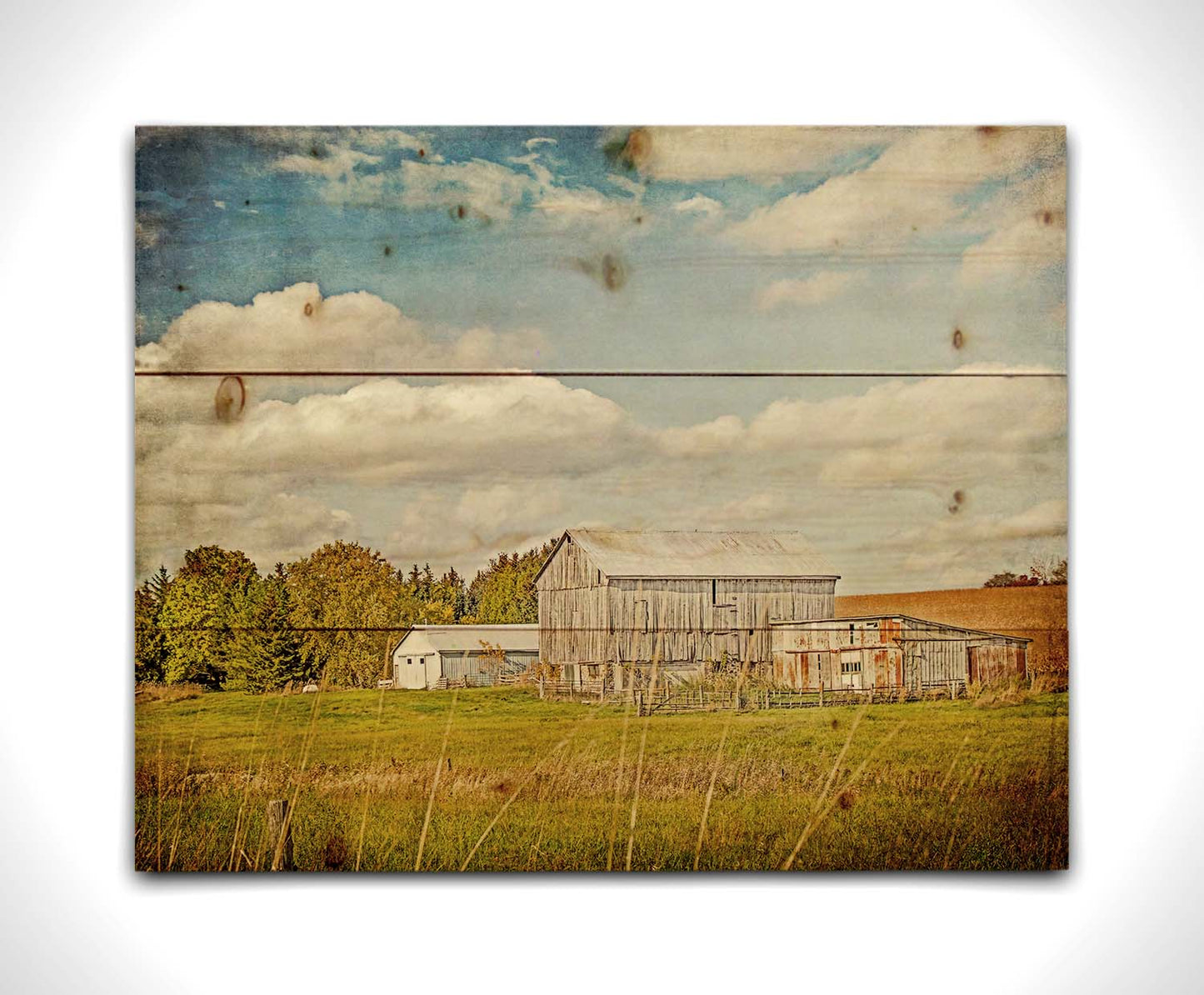 A photo of several barns, their associated pastures, and fields. The early signs of fall are present in the steadily changing leaves and crops. The sky above is wide, blue, and populated with fluffy clouds. Printed on a wood pallet.