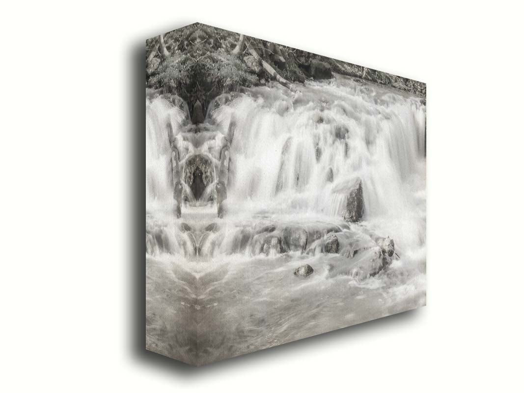 A grayscale photograph of a small river waterfall, only a few feet high. The use of a slow shutter speed technique gives the water a soft, gentle appearance. Printed on canvas.