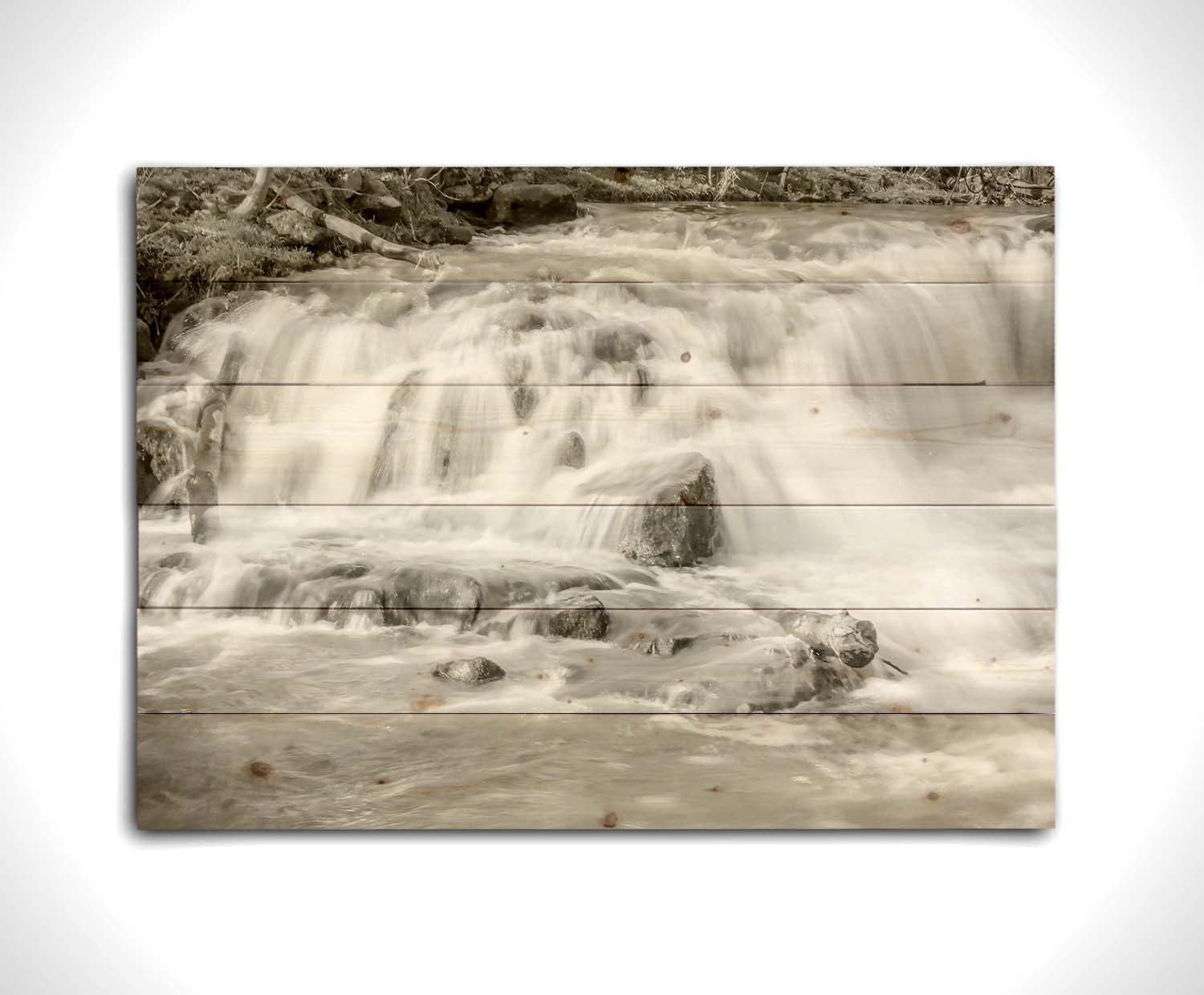 A grayscale photograph of a small river waterfall, only a few feet high. The use of a slow shutter speed technique gives the water a soft, gentle appearance. Printed on a wood pallet.