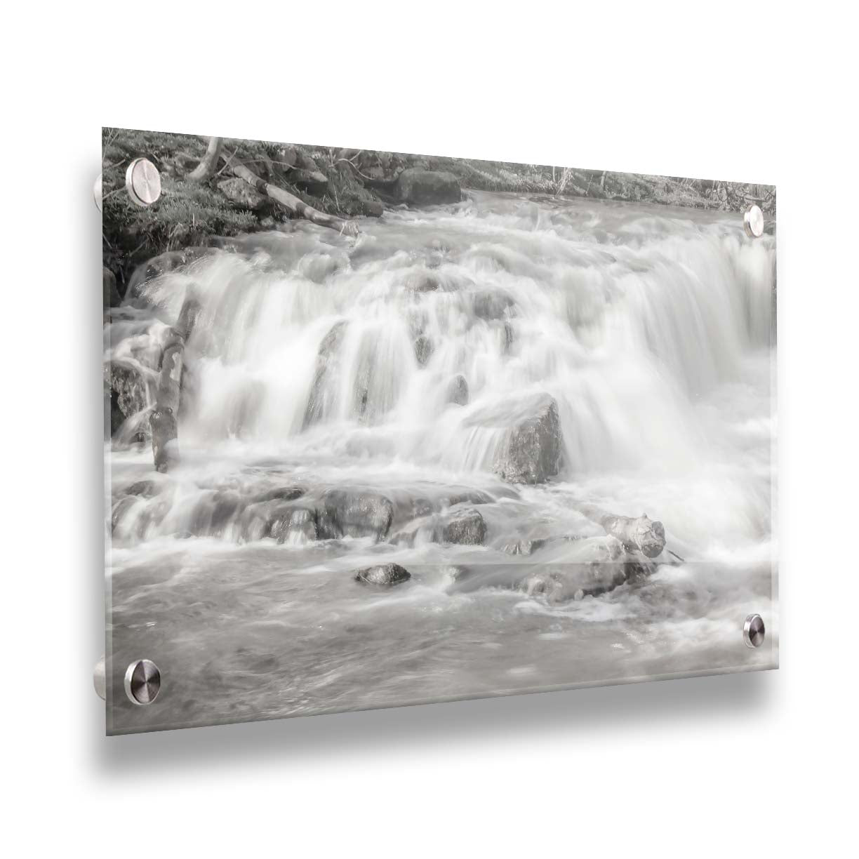 A grayscale photograph of a small river waterfall, only a few feet high. The use of a slow shutter speed technique gives the water a soft, gentle appearance. Printed on acrylic.