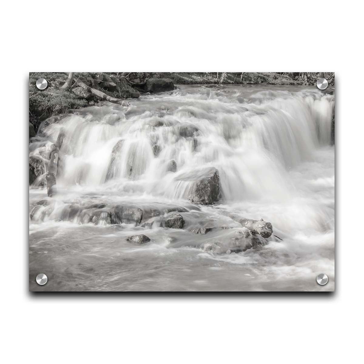 A grayscale photograph of a small river waterfall, only a few feet high. The use of a slow shutter speed technique gives the water a soft, gentle appearance. Printed on acrylic.