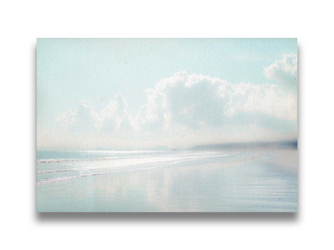 A photo of a beach on a bright but foggy day. The light reflects on the wet sand with the color of the sky,, adding to the dreamlike appearance. A city can be seen through the fog in the distance. Printed on canvas.