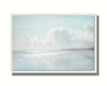 A photo of a beach on a bright but foggy day. The light reflects on the wet sand with the color of the sky,, adding to the dreamlike appearance. A city can be seen through the fog in the distance. Printed on canvas in a float frame.