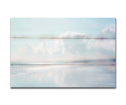 A photo of a beach on a bright but foggy day. The light reflects on the wet sand with the color of the sky,, adding to the dreamlike appearance. A city can be seen through the fog in the distance. Printed on a box board.