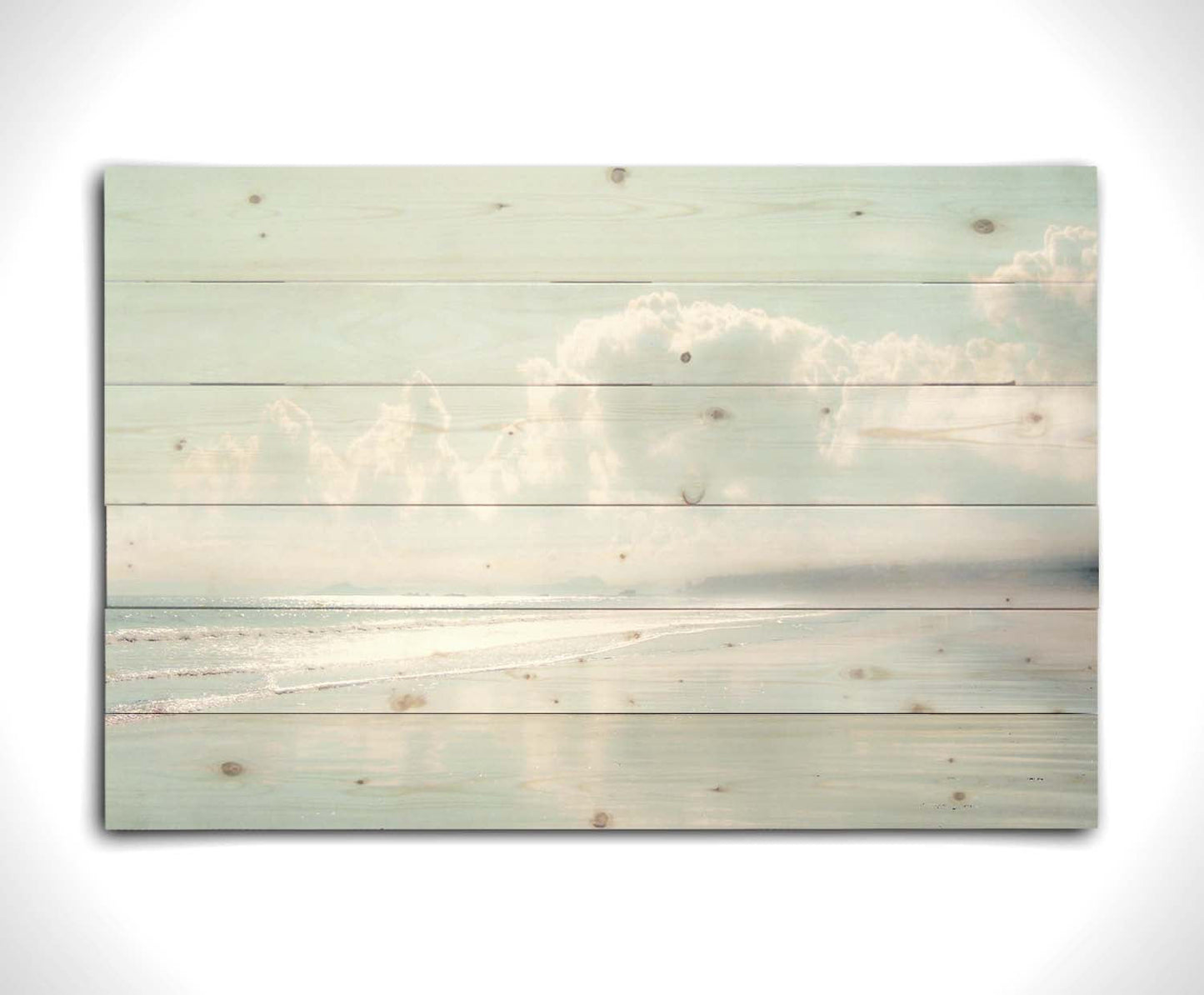 A photo of a beach on a bright but foggy day. The light reflects on the wet sand with the color of the sky,, adding to the dreamlike appearance. A city can be seen through the fog in the distance. Printed on a wood pallet.