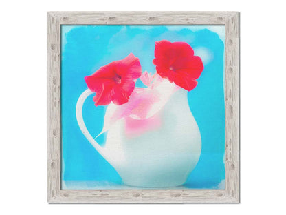 A photo of two red flowes in a white pitcher vase against a cyan backgrround. Printed on canvas and framed.