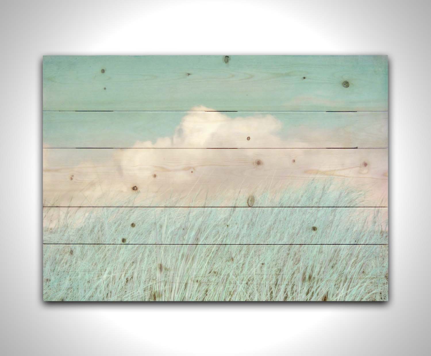 A photo of tall grass under a blue sky with white clouds. Printed on a wood pallet.