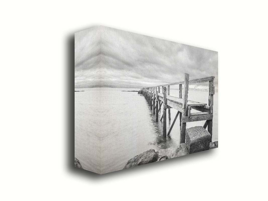 A grayscale photograph of an old wooden pier in Scotland, stretching away from the rocky shore into the waters. Printed on canvas.