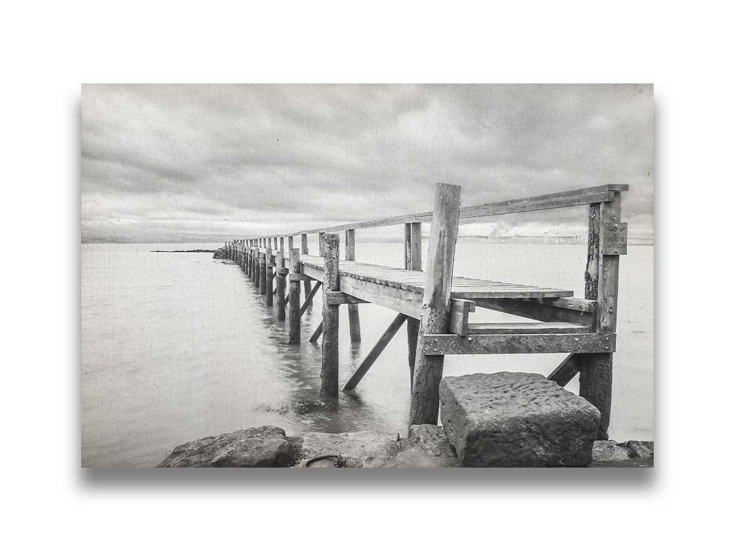 A grayscale photograph of an old wooden pier in Scotland, stretching away from the rocky shore into the waters. Printed on canvas.