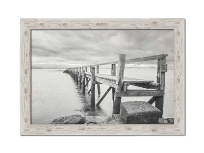 A grayscale photograph of an old wooden pier in Scotland, stretching away from the rocky shore into the waters. Printed on canvas and framed.