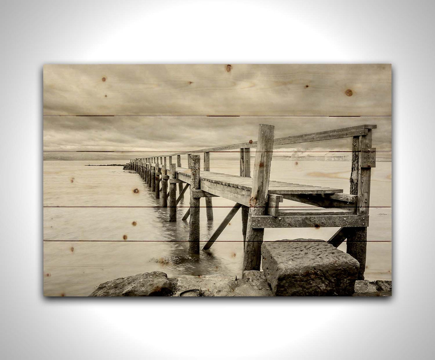 A grayscale photograph of an old wooden pier in Scotland, stretching away from the rocky shore into the waters. Printed on a wood pallet.