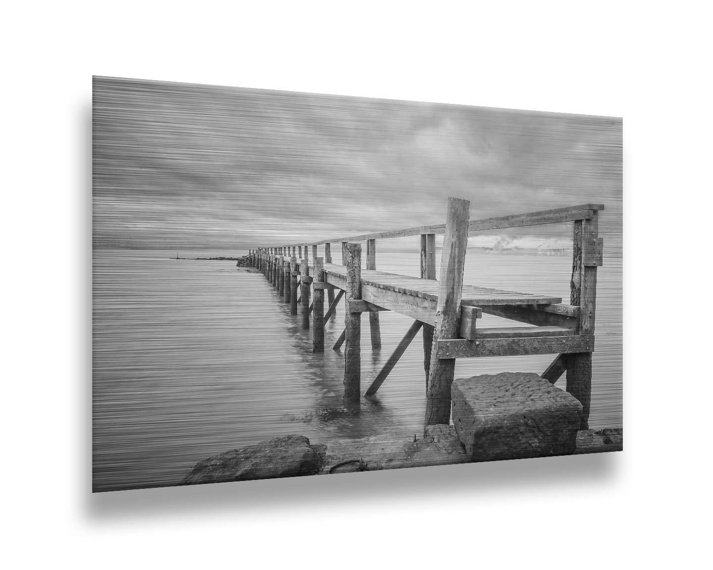 A grayscale photograph of an old wooden pier in Scotland, stretching away from the rocky shore into the waters. Printed on metal.