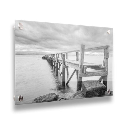 A grayscale photograph of an old wooden pier in Scotland, stretching away from the rocky shore into the waters. Printed on acrylic.