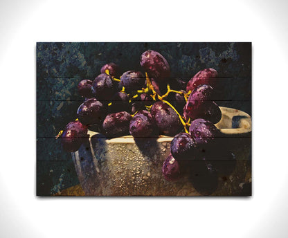 A photo of a bunch of purple grapes in a bowl, covered in drops of water and overlayed with textues. Printed on a wood pallet.