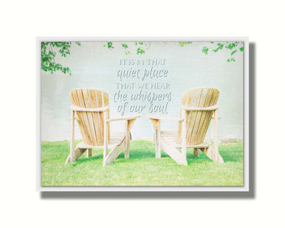 A photo of two wood lawn chairs, sitting on bright green grass, facing a lake. It is overlaid with the phrase, "It is in that quiet place that we hear the whispers of our soul." Printed on canvas in a float frame.