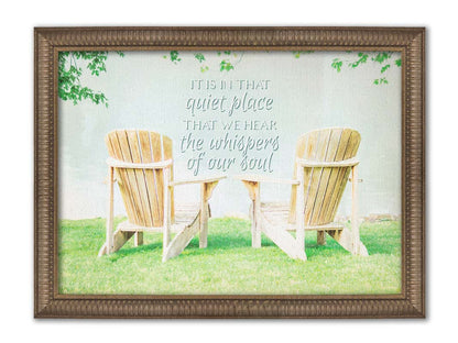 A photo of two wood lawn chairs, sitting on bright green grass, facing a lake. It is overlaid with the phrase, "It is in that quiet place that we hear the whispers of our soul." Printed on canvas and framed.