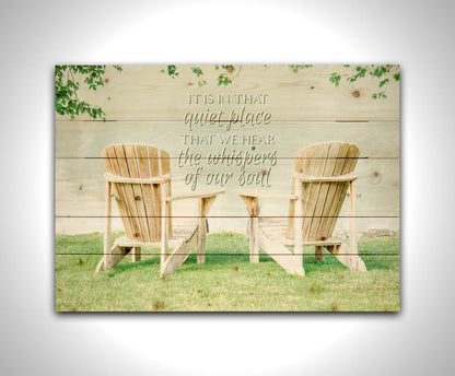 A photo of two wood lawn chairs, sitting on bright green grass, facing a lake. It is overlaid with the phrase, "It is in that quiet place that we hear the whispers of our soul." Printed on a wood pallet.