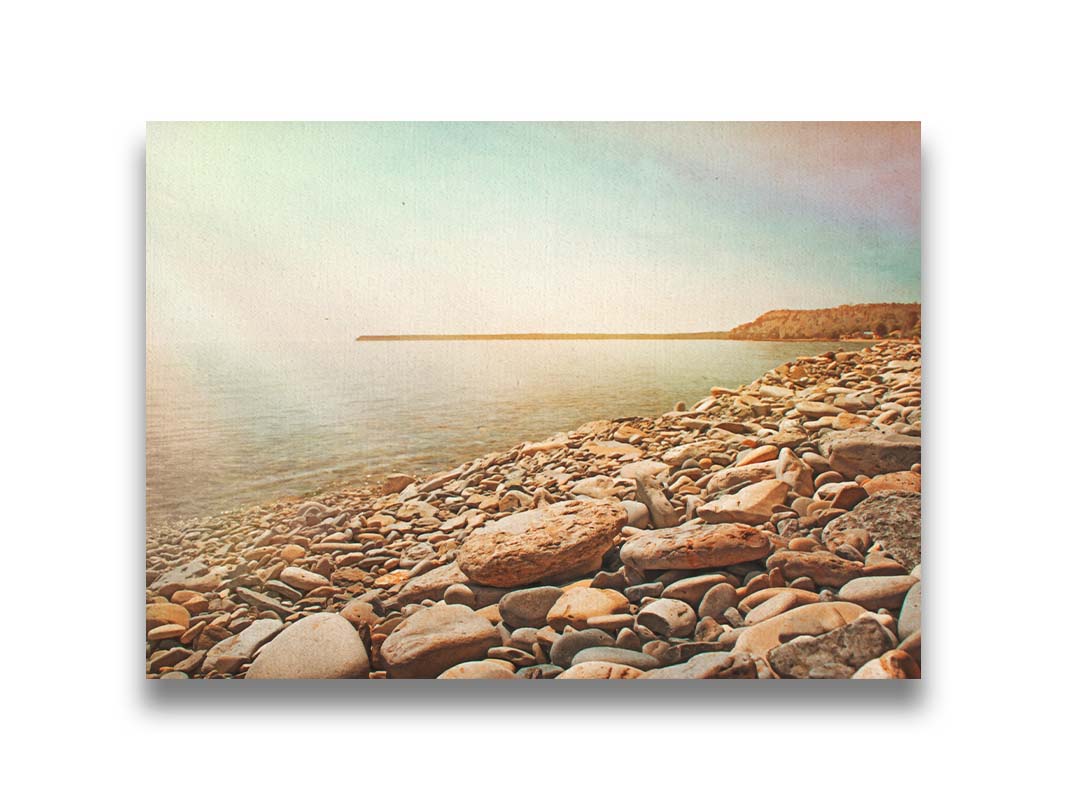 A warm-colored photograph of a rocky beach in the sunlight, bathed in a spectrum of colors. Printed on canvas.