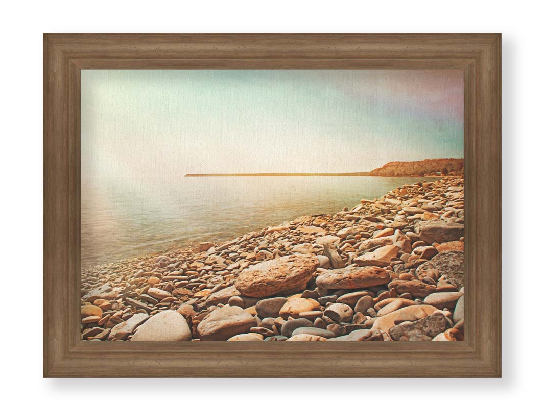 A warm-colored photograph of a rocky beach in the sunlight, bathed in a spectrum of colors. Printed on canvas and framed.