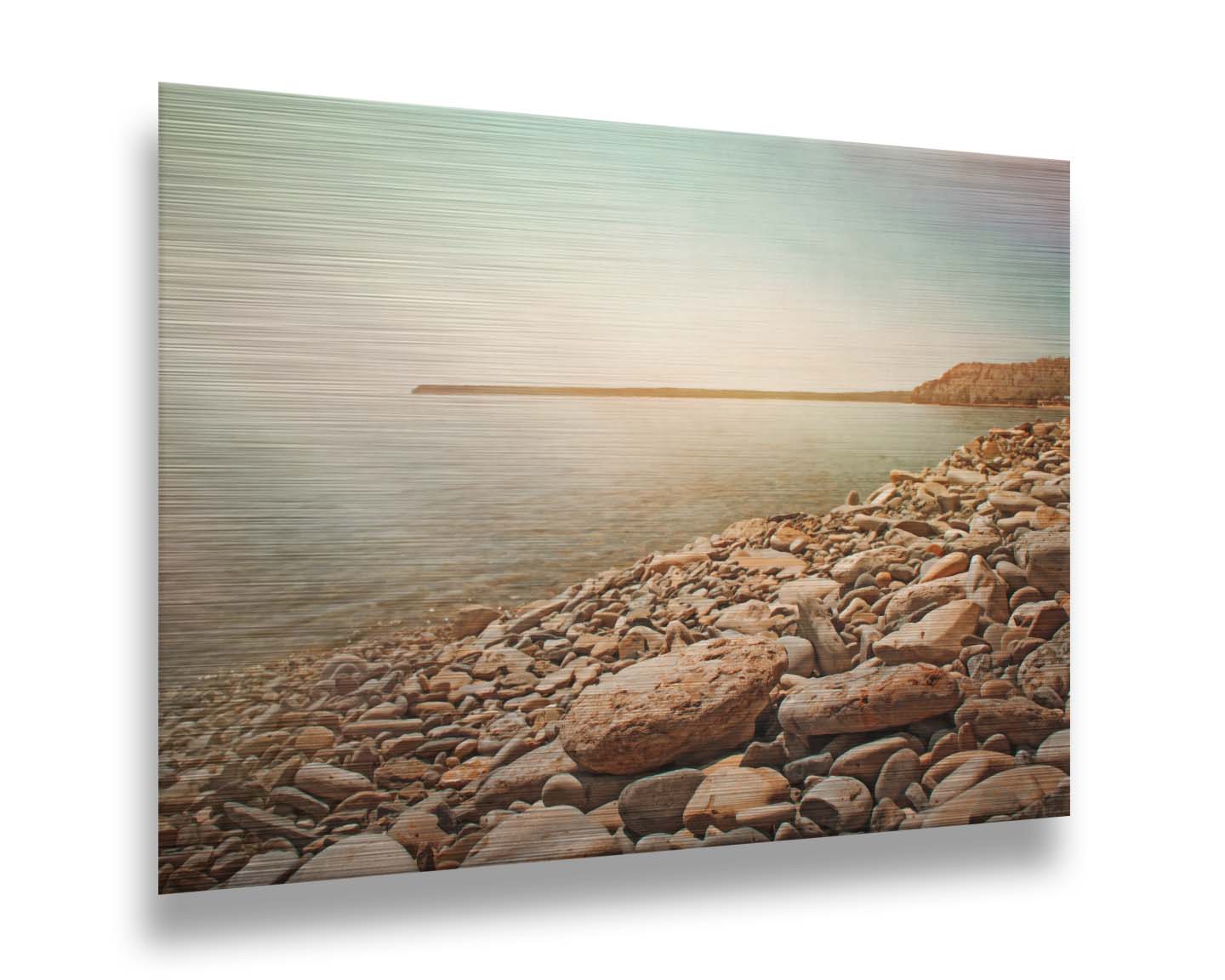 A warm-colored photograph of a rocky beach in the sunlight, bathed in a spectrum of colors. Printed on metal.