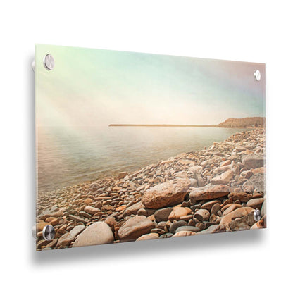 A warm-colored photograph of a rocky beach in the sunlight, bathed in a spectrum of colors. Printed on acrylic.