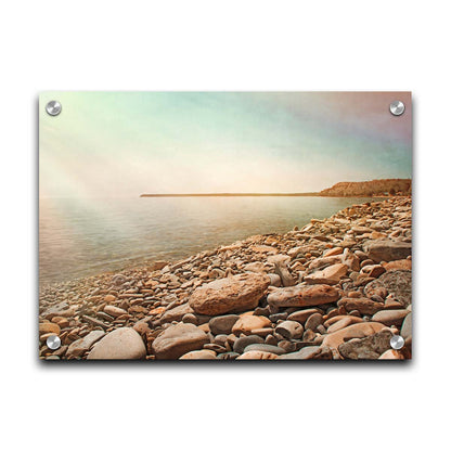 A warm-colored photograph of a rocky beach in the sunlight, bathed in a spectrum of colors. Printed on acrylic.