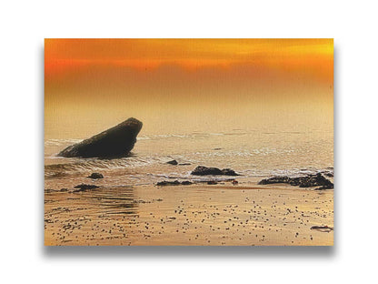 A photo on a beach, looking out at rocks jutting out from the sea against an orange sunset. Printed on canvas.