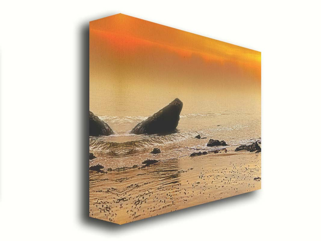 A photo on a beach, looking out at rocks jutting out from the sea against an orange sunset. Printed on canvas.