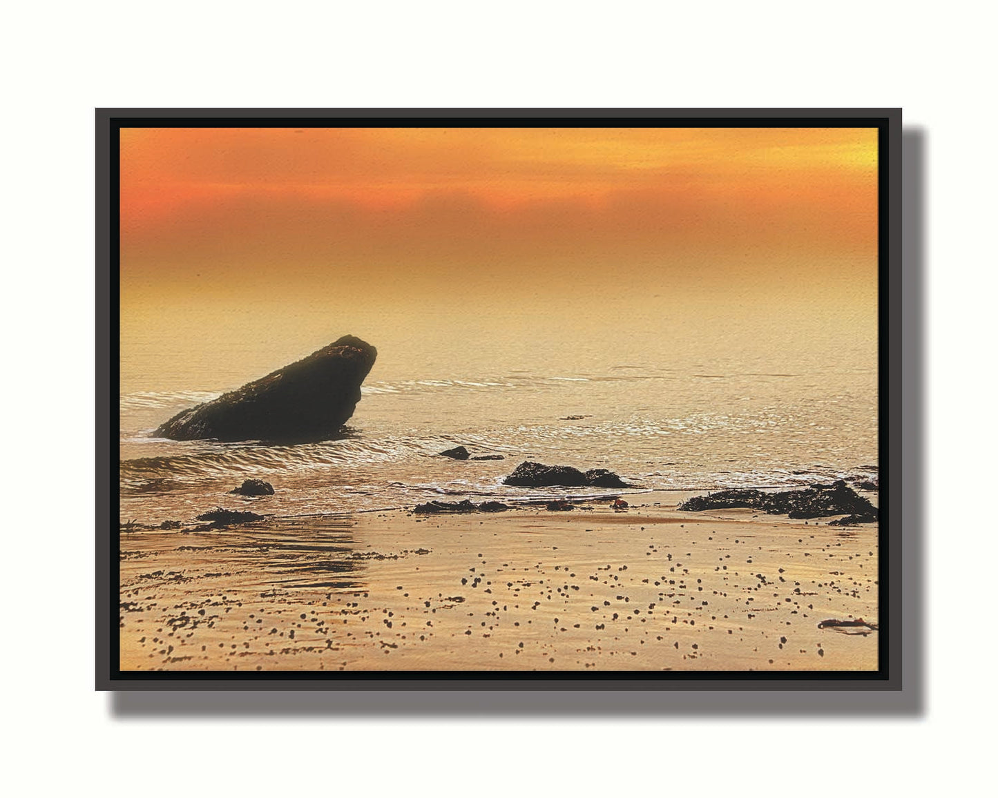 A photo on a beach, looking out at rocks jutting out from the sea against an orange sunset. Printed on canvas in a float frame.