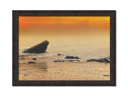 A photo on a beach, looking out at rocks jutting out from the sea against an orange sunset. Printed on canvas and framed.