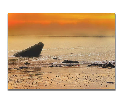 A photo on a beach, looking out at rocks jutting out from the sea against an orange sunset. Printed on a box board.