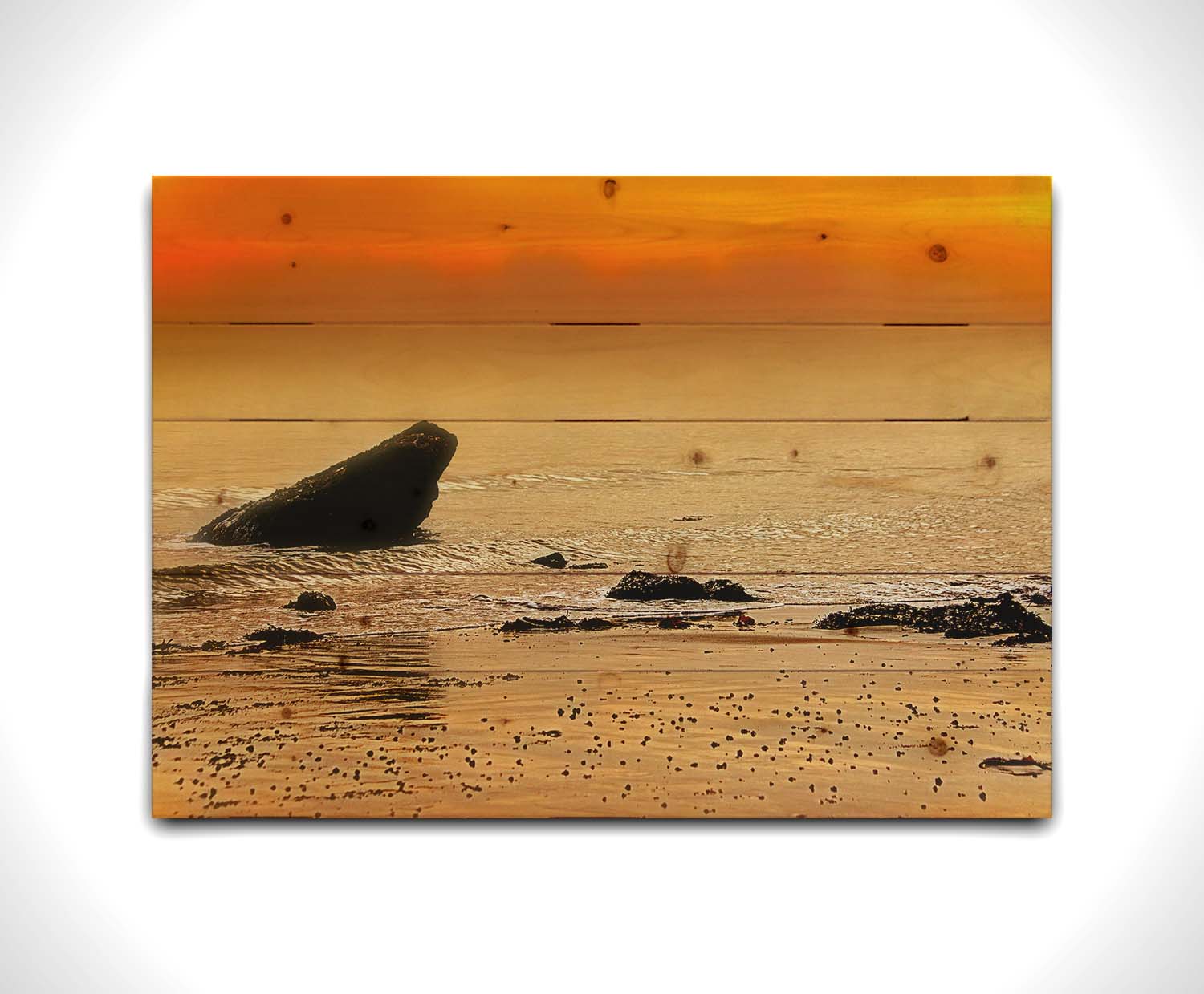 A photo on a beach, looking out at rocks jutting out from the sea against an orange sunset. Printed on a wood pallet.