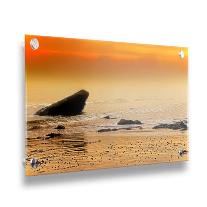 A photo on a beach, looking out at rocks jutting out from the sea against an orange sunset. Printed on acrylic.