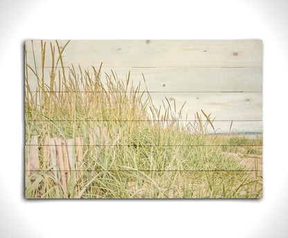 A photograph of tall grasses at the beach, surrounding a short wooden fence. Printed on a wood pallet.