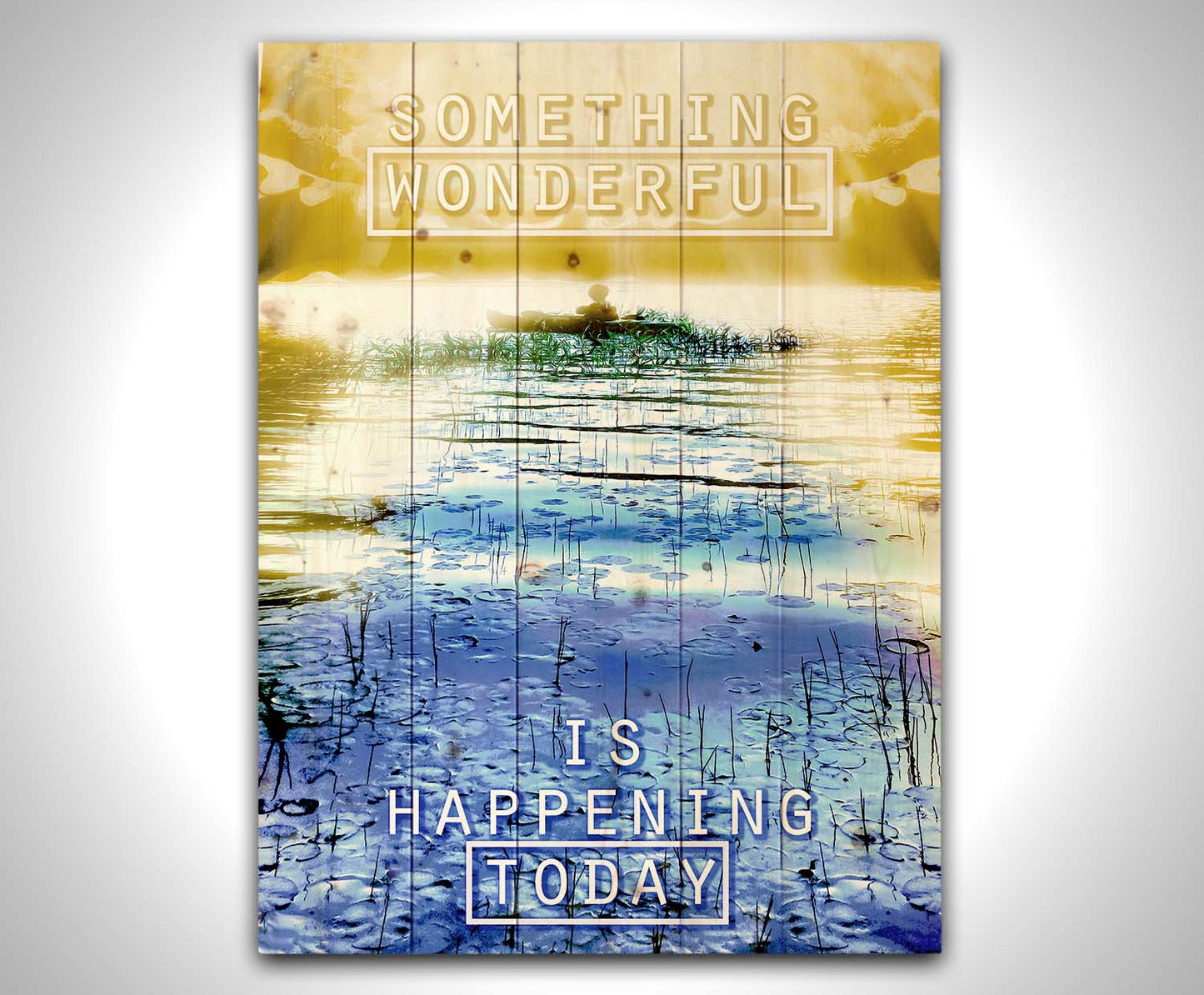 An edited photo graphic depicting a person in a canoe on a lake. It is bathed in yellow light, contrasted by the bright blue water. It is overlaid with the phrase "Something wonderful is happening today." Printed on a wood pallet.